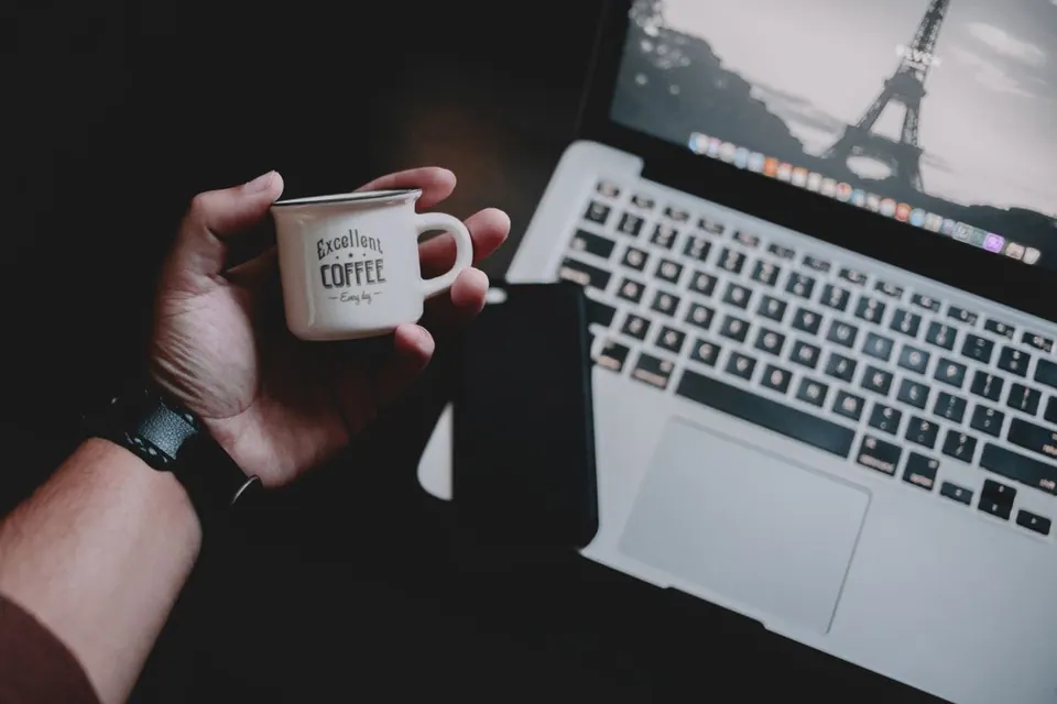 Người dùng cầm ly cà phê ngay cạnh MacBook đang mở