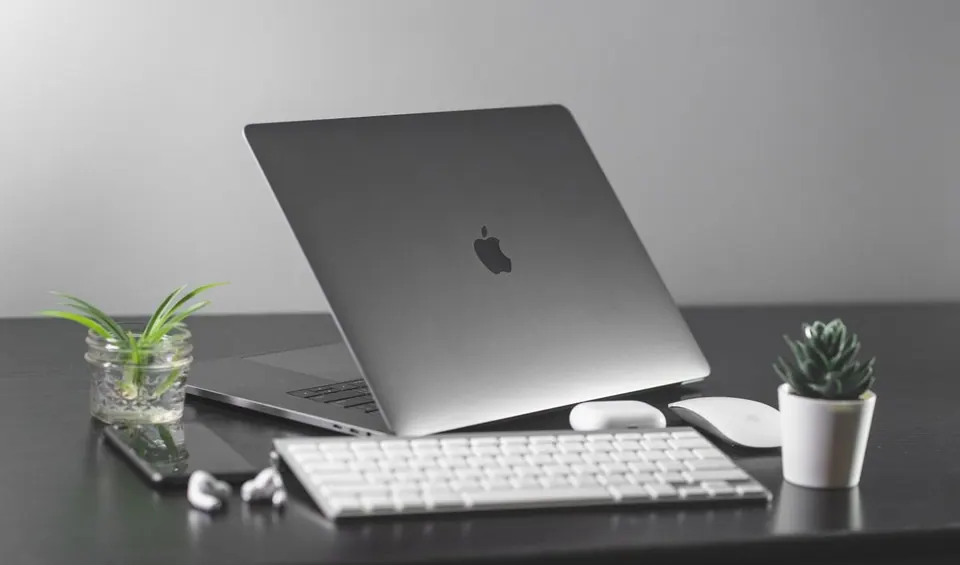 MacBook đặt trên bàn làm việc tối giản cùng bàn phím và chuột rời