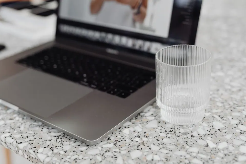 MacBook đặt cạnh cốc nước trên bàn làm việc